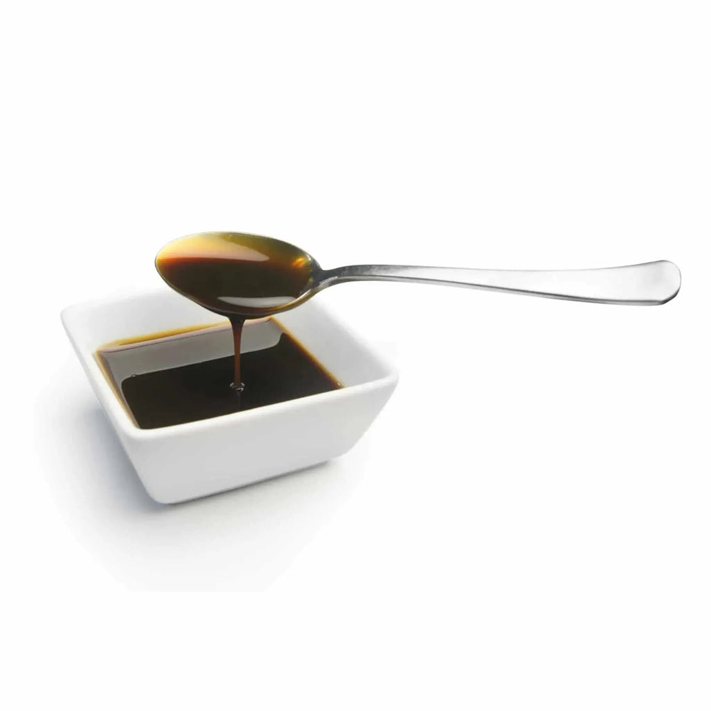 Spoon pouring dark liquid into a small white bowl on a white background