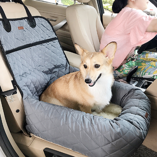 Dog sitting in a car seat cover in a vehicle with a person in the background.