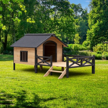 Wooden pet house with a black roof on a grassy area with trees in the background