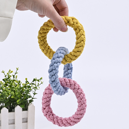 Three braided pet toys in yellow, blue, and pink held by a hand with a white background.