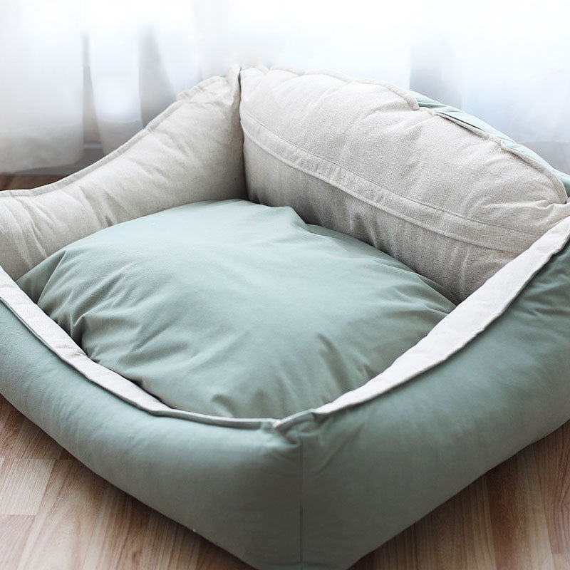 Pet bed with two cushions, one beige and one light green, on a wooden floor.