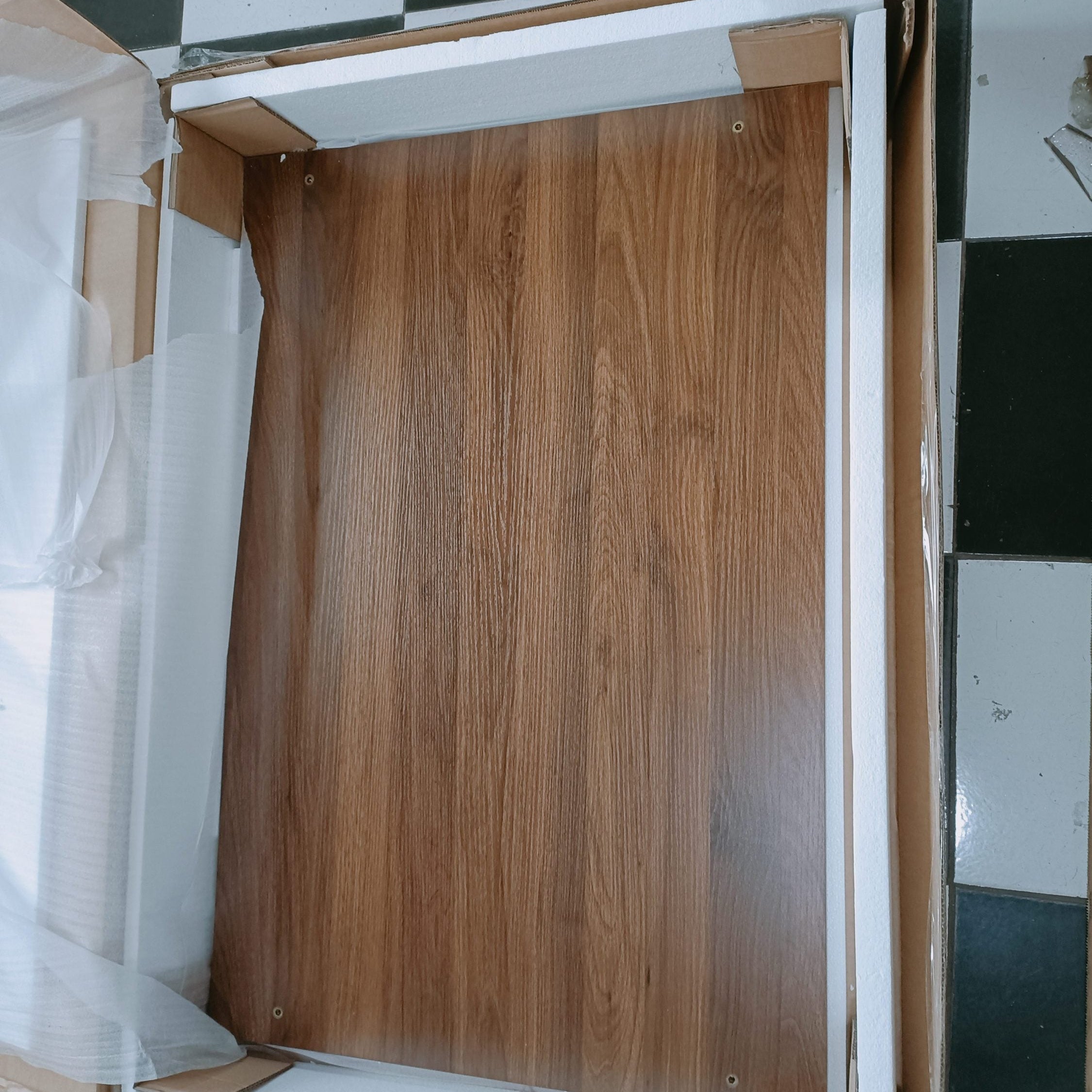 Wooden panel in a cardboard box on a checkered floor