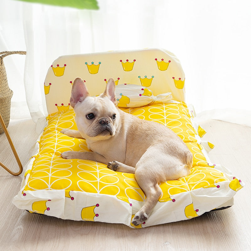 Dog lying on a yellow and white patterned pet bed with a small table in the background.