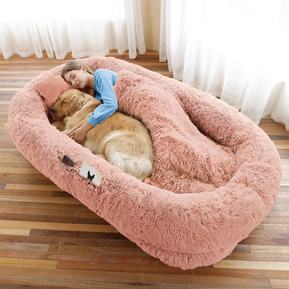 Person lying on a fluffy pink pet bed with a dog, surrounded by white curtains.