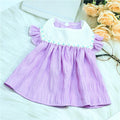 Purple checkered  dog dress on a white surface with flowers and glasses in the background