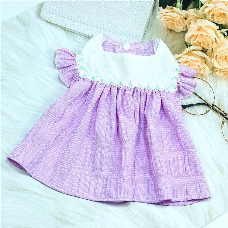 Purple checkered  dog dress on a white surface with flowers and glasses in the background