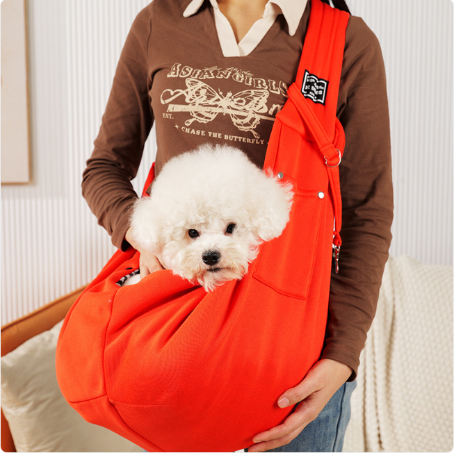 Person holding a small white dog in an orange pet sling against a neutral background