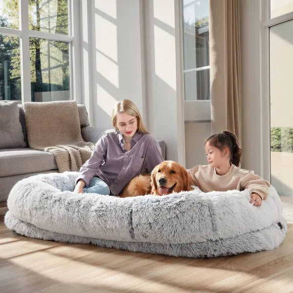 Two children and a dog on a large fluffy pet bed in a bright living room.