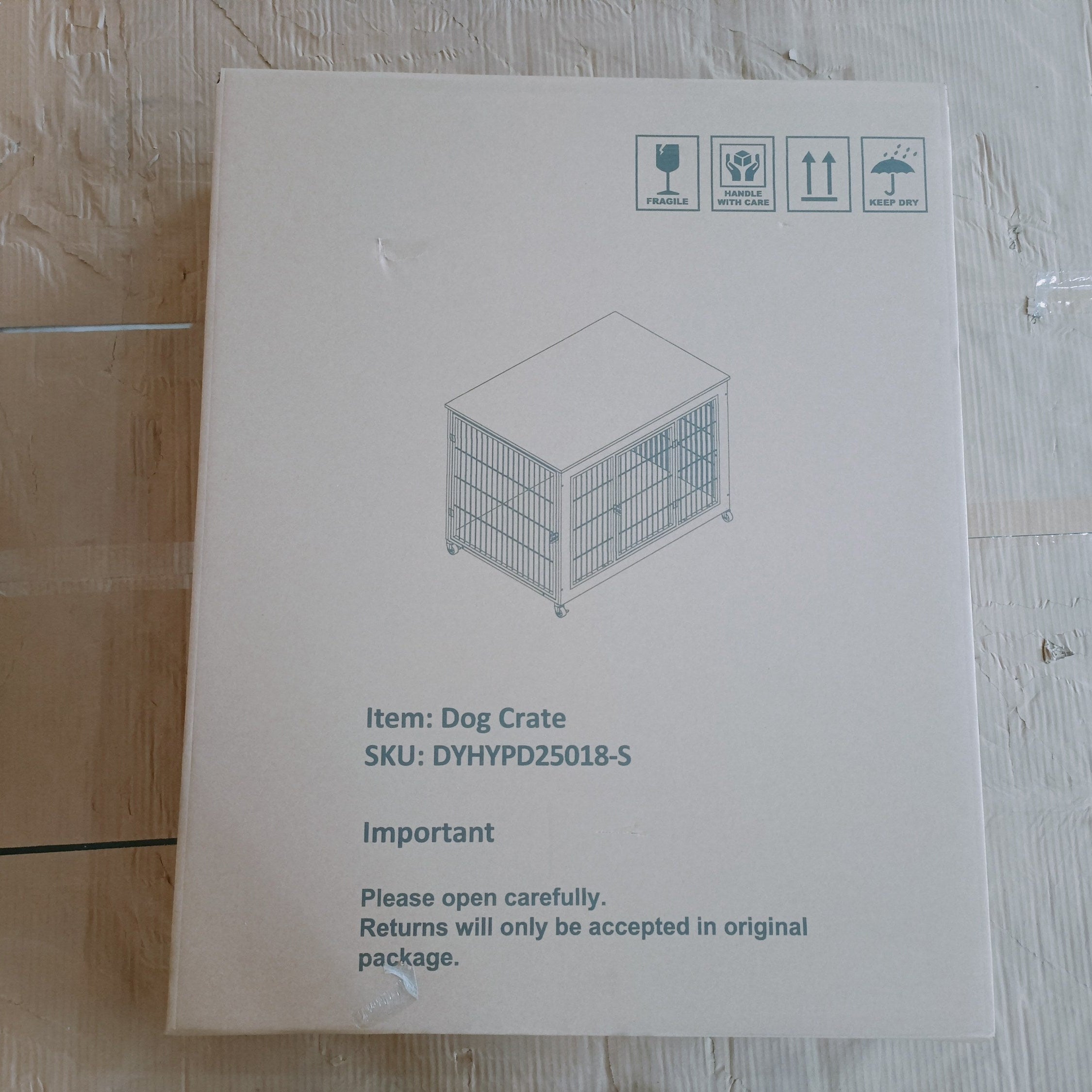 Cardboard box with a dog crate illustration and text on a wooden floor.