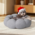 Dog wearing a Santa hat on a fluffy gray pet bed in a cozy room.