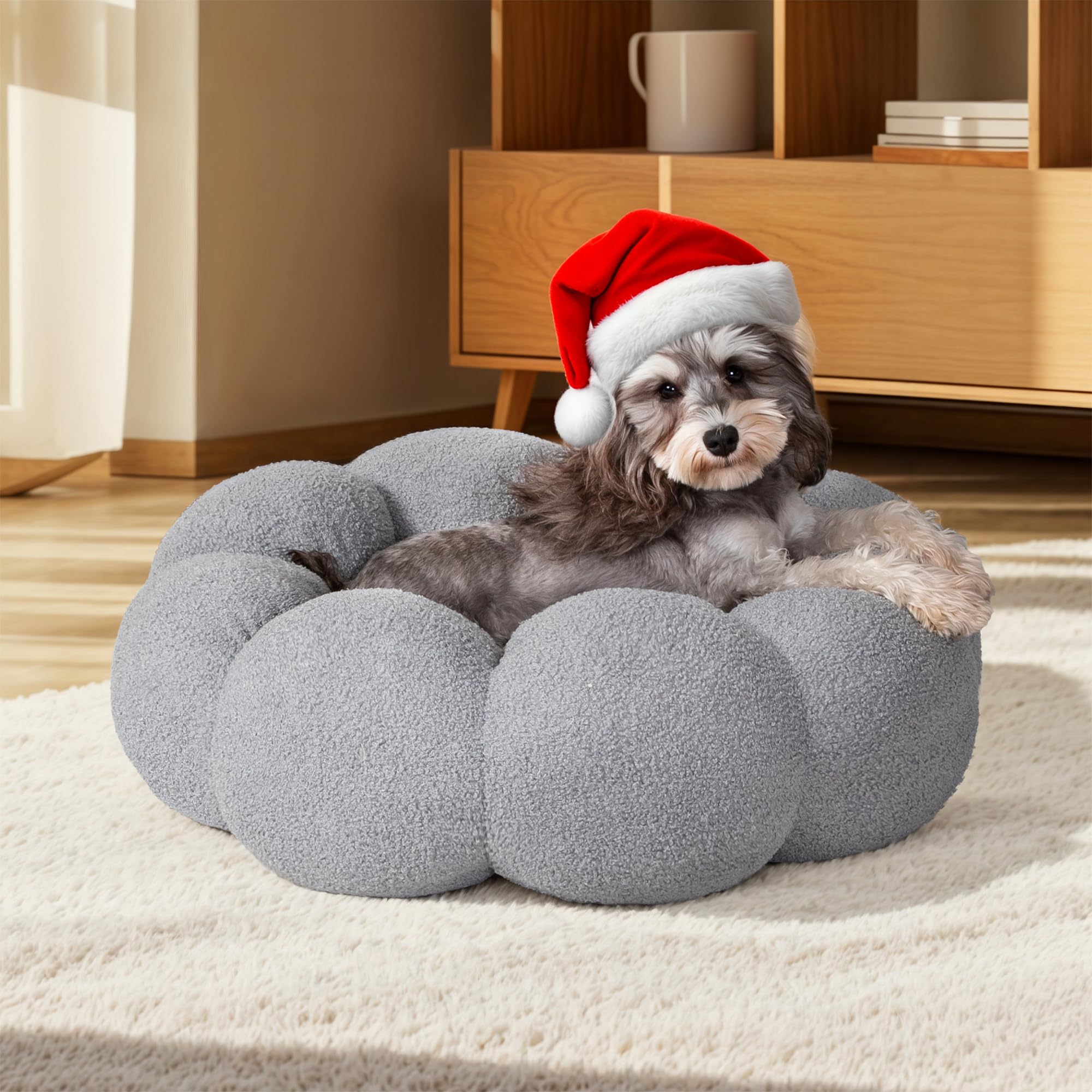 Dog wearing a Santa hat on a fluffy gray pet bed in a cozy room.
