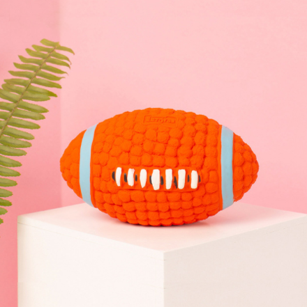 Orange textured football-shaped toy on a pink background with a green leaf