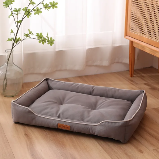 Gray pet bed on a wooden floor with a vase and plant in the background