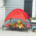 Dog lying on a red pet cot with canopy in an outdoor setting