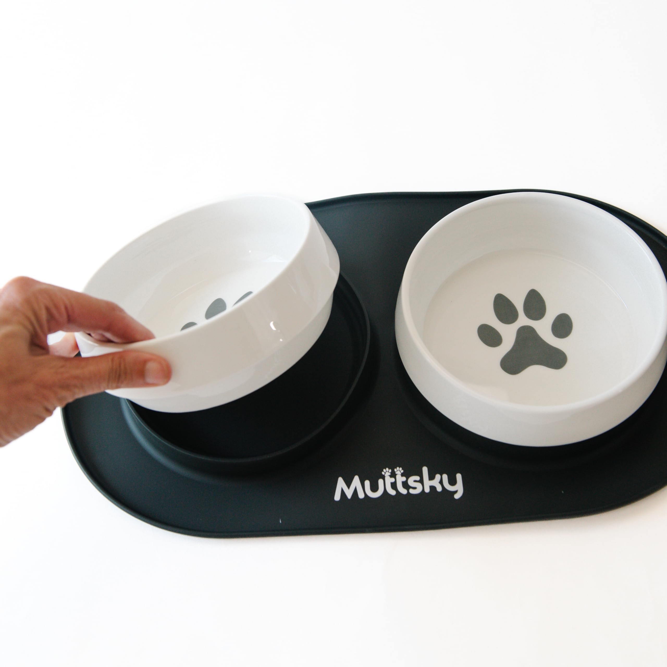 Pet bowls with a paw print design on a black mat, held by a hand.