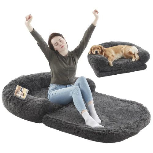 Person sitting on a large gray pet bed with a smaller dog bed and dog in the background.