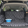 Car trunk with a black and white paw print cover and a blue bowl inside.