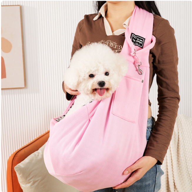 Person holding a small white dog in a pink sling against a neutral background